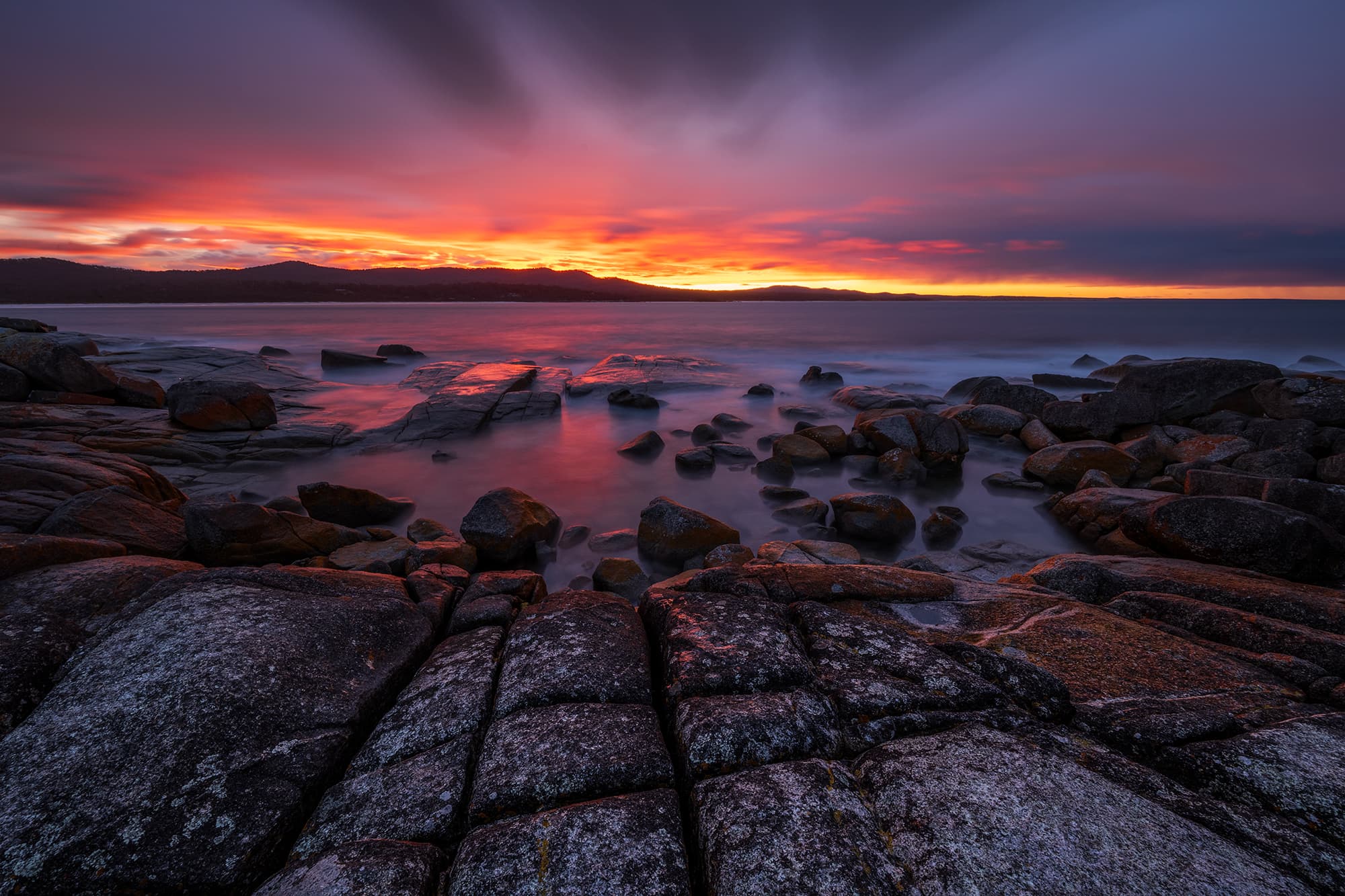 Fiery orange lichen-covered rocks at the Bay of Fires, Tasmania