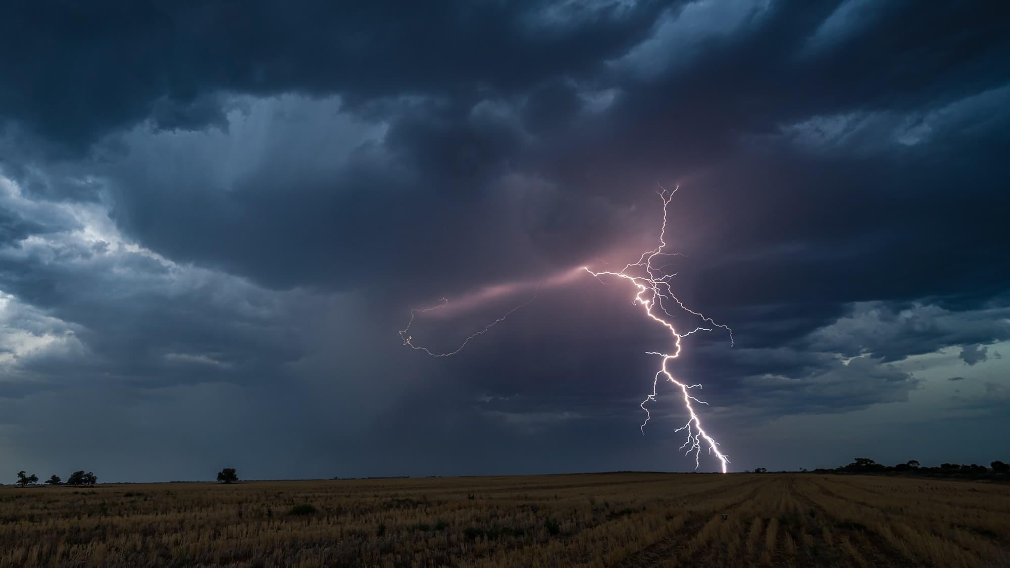 A hammer-shaped lightning bolt striking over flat Victorian farmland